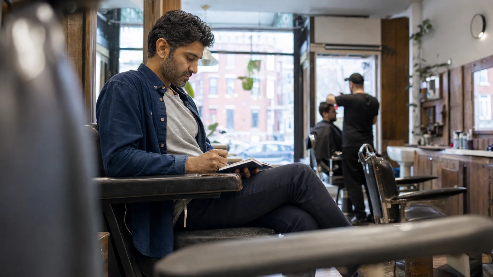 A middle-aged man writes a few private notes while waiting in a Montréal neighbourhood barbershop before an appointment.