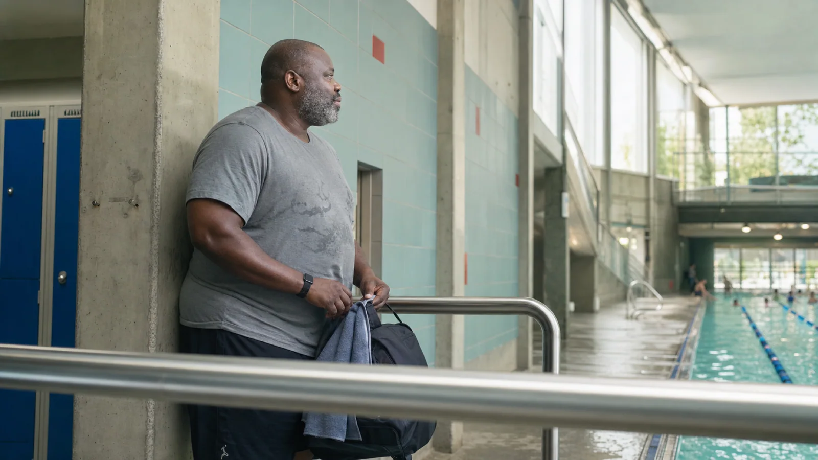 A middle-aged man pauses in side profile beside a Montréal public pool after an aquafitness session.